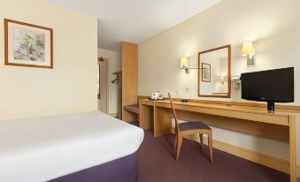 a hotel room with a bed , desk , and chair , as well as a mirror on the wall at Days Inn by Wyndham Sevenoaks Clacket Lane