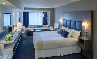 a large bed with white linens is in a room with a couch , chair , and lamps at Novotel Montréal Centre