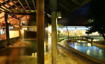 a nighttime scene of a man swimming in a pool , surrounded by lush greenery and a building in the background at Rainbow Hotel