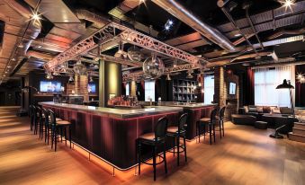 a modern bar with wooden flooring , black chairs , and a large bar counter under a metal canopy at Ginn Hotel Berlin Potsdam