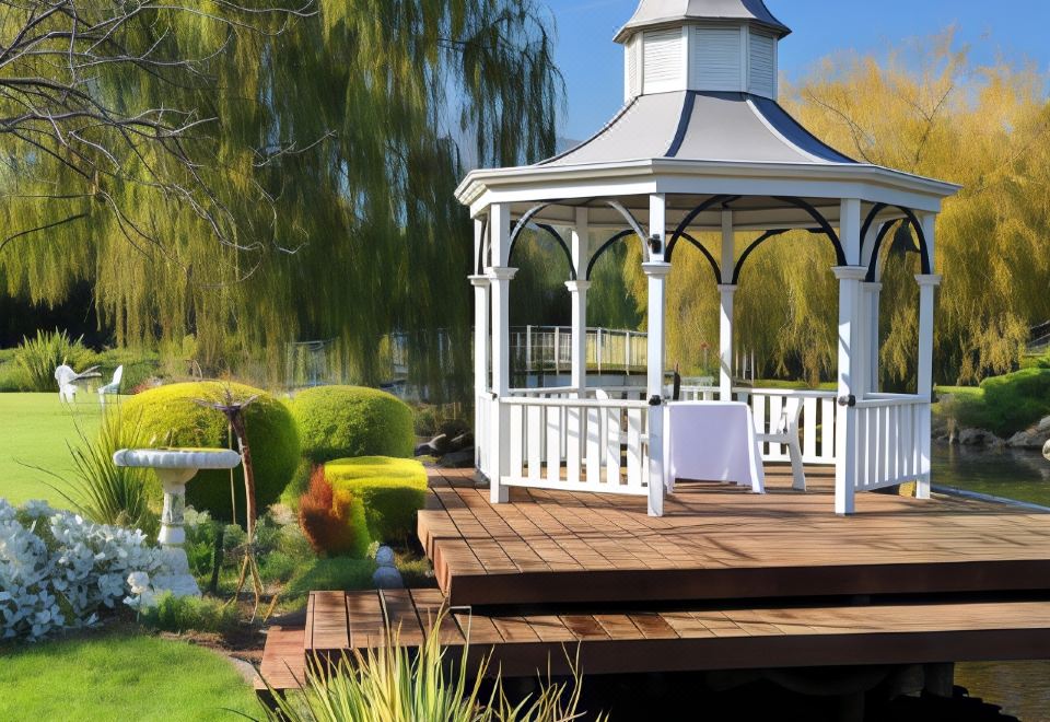 a white gazebo surrounded by a wooden deck , with a fountain in the background and trees in the foreground at Lakeside Cottage Luxury B&B