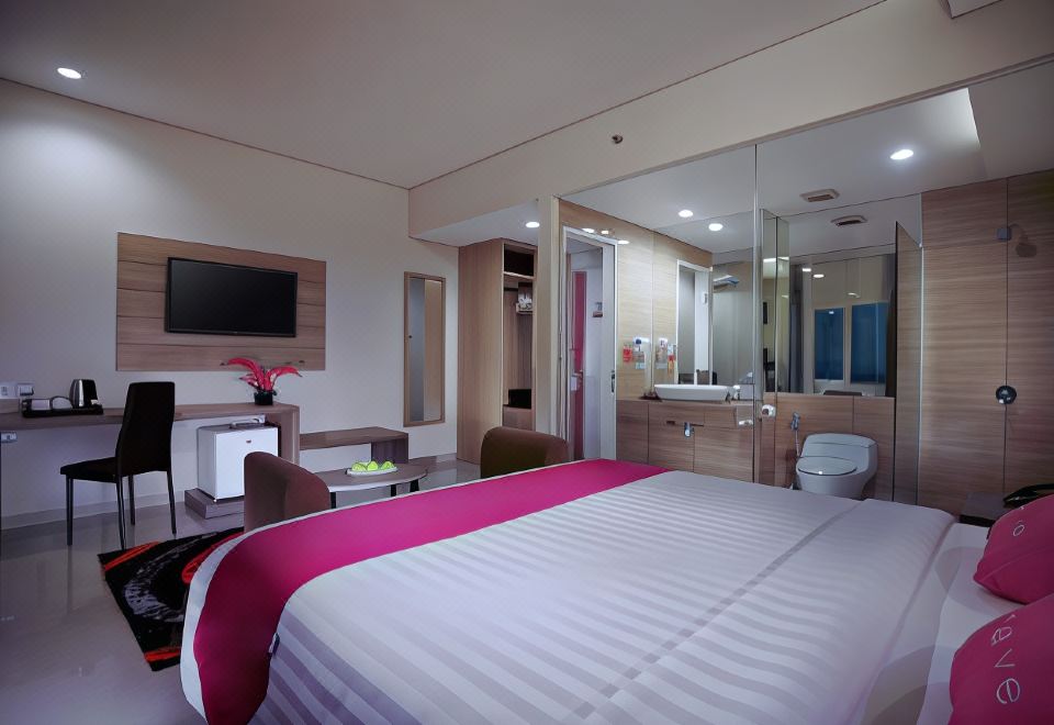 a hotel room with a large bed , a bathroom with a bathtub , and a television at favehotel Langko Mataram - Lombok