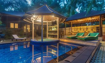 a tropical villa with a pool and a bar , surrounded by palm trees at night at Coconut Boutique Resort