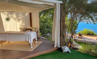 a luxurious bedroom with a large bed and a hammock on a deck overlooking the ocean at A’mare Corsica Seaside Small Resort