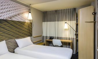 a modern hotel room with a white bed , desk , and chair , as well as a window with a gray curtain at Ibis Guaiba