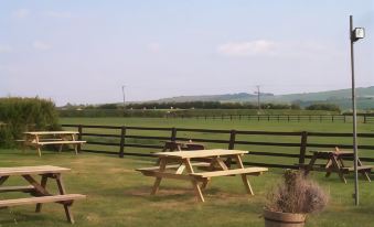 a wooden picnic table and benches in a grassy field , with a fence surrounding the area at The Fox & Hounds