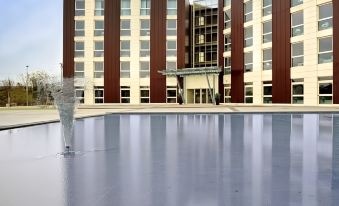 a large outdoor pool is surrounded by a modern building with a fountain in the center at Idea Hotel Milano Malpensa Airport