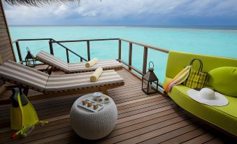 a wooden deck with lounge chairs and a green chair , overlooking the ocean , is furnished with various items such as pillows and a coffee table at Outrigger Maldives Maafushivaru Resort