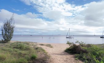 a beach scene with a sailboat in the water and people walking along the shore at 1770 Beach Shacks