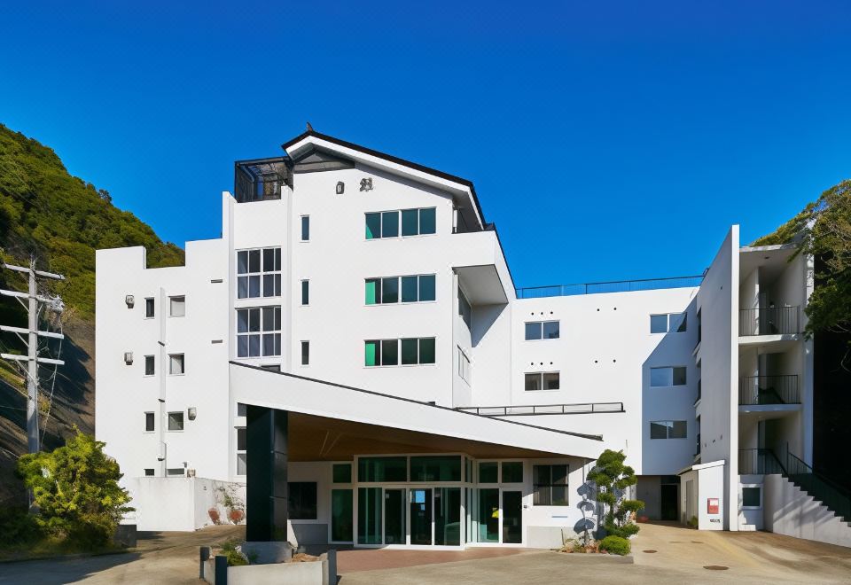 a modern white building with a sloping roof and large windows , surrounded by trees and plants at Hakugei