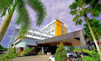 a modern building with a yellow facade and white roof , surrounded by palm trees and cars at Aquarius Boutique Hotel Sampit