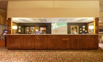 a hotel lobby with a wooden reception desk , carpeted floor , and a large screen on the wall at Best Western Plus Madison-Huntsville Hotel