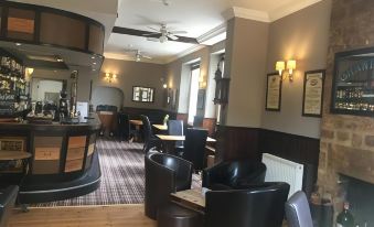 a bar area with black leather chairs , wooden floors , and a glass counter , as well as a couch and dining table at The White Hart Hotel