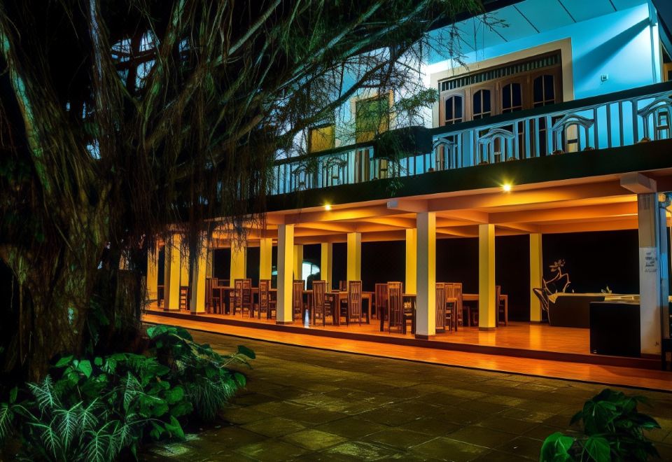 an outdoor dining area with wooden tables and chairs , surrounded by trees and lit up at night at Rainforest Lodge, Deniyaya