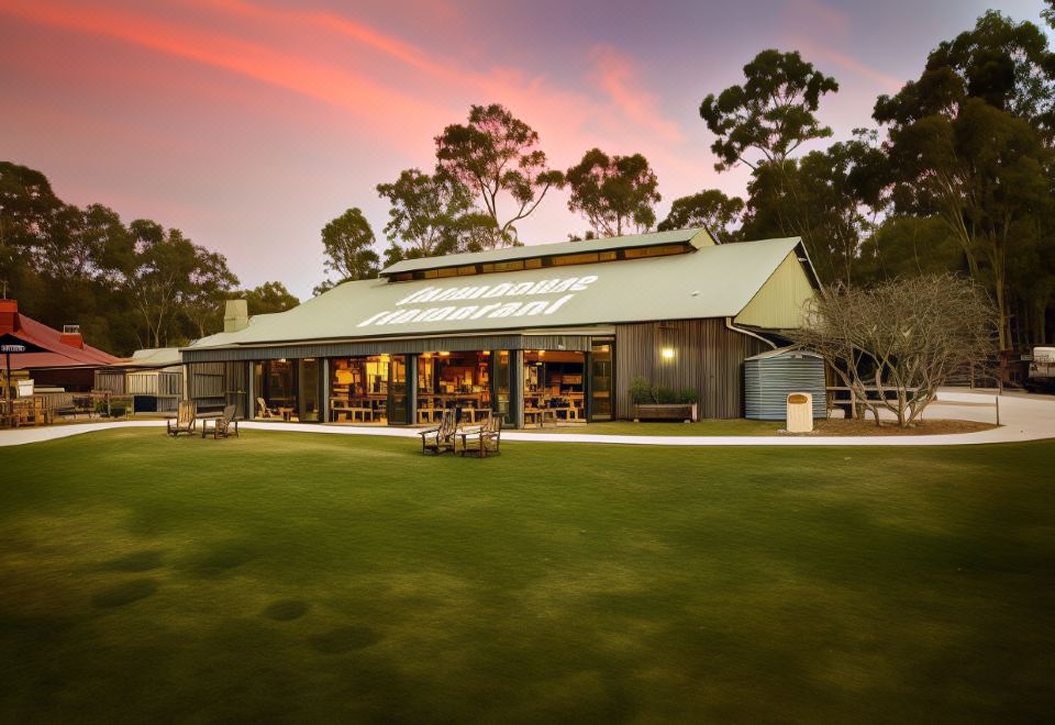 a large building with a green lawn and trees in the background , under a pink sky at Paradise Country Farmstay