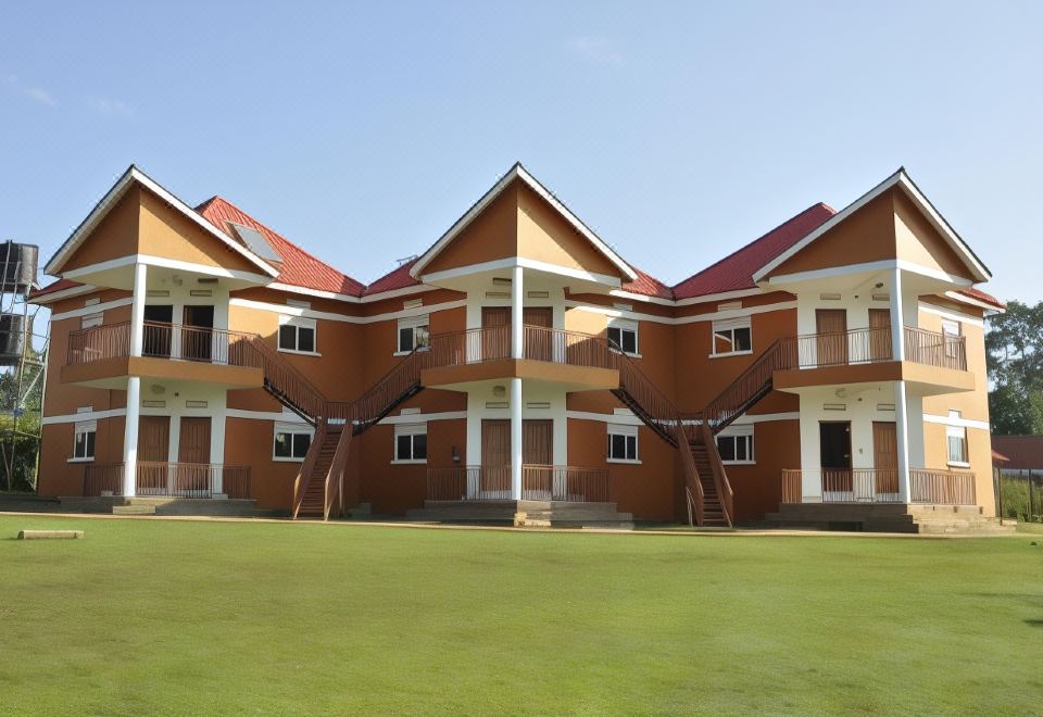 a large , multi - story building with a red roof and white walls is surrounded by a green lawn at Country Inn Masindi