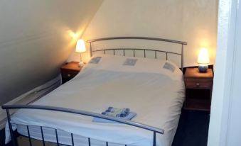 a bed with white sheets and a metal headboard is flanked by two lamps on either side at Three Horseshoes Inn