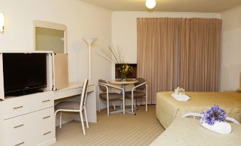 a modern hotel room with a white desk , a bed , and a television , all set against a beige - colored wall at Bankstown Motel 10