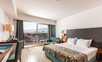 a modern hotel room with a large bed , two chairs , and a balcony overlooking the city at Palm Wings Kusadasi Beach Resort&Spa