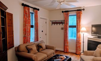 a cozy living room with a brown couch , wooden coffee table , and orange curtains near a window at The Inn at Montchanin Village