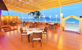 a large dining room with wooden floors and tables set for a meal , overlooking the ocean at Bluebay Beach Resort