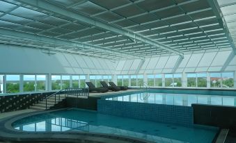 a large swimming pool with a curved edge and lounge chairs is surrounded by a glass ceiling at Aquarius Boutique Hotel Sampit