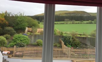 a view of a green field and a body of water from an open window at The Border Hotel