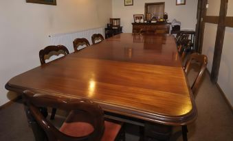 a large wooden dining table surrounded by chairs in a room with a fireplace and paintings on the wall at Bluebell Farm