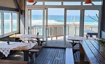 a dining room with a wooden table and chairs , overlooking the ocean through large windows at Umkomaas Lodge