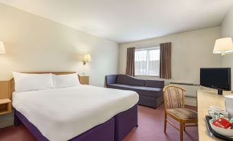 a large bed with a purple skirt is in the middle of a room with a window and a chair at Days Inn by Wyndham Chesterfield Tibshelf