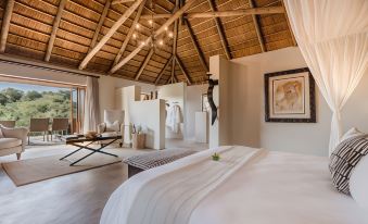 a luxurious bedroom with a large bed , white bedding , and a wooden ceiling decorated with lights at Bukela Game Lodge - Amakhala Game Reserve