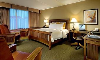 a hotel room with a king - sized bed , two nightstands , and a desk , all set against a backdrop of windows at DoubleTree by Hilton Hotel Libertyville - Mundelein