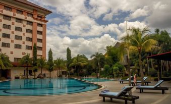 a large swimming pool with lounge chairs and palm trees in front of a building at The Sunan Hotel Solo