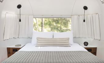 a white bed with a striped blanket and two pillows is in a room with large windows at AutoCamp Yosemite