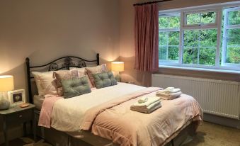 a neatly made bed with pink linens is situated in a room next to a window at Leafy Suburban Bed and Breakfast