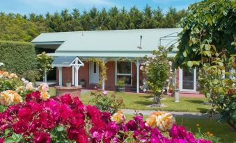 a large house with a green roof and white trim is surrounded by pink and purple flowers at Lakeside Cottage Luxury B&B