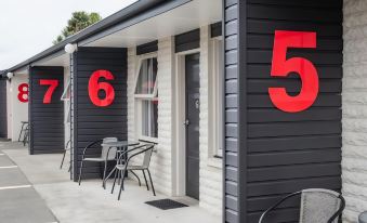 a black house with red numbers on its exterior , including numbers 6 and 5 , accompanied by chairs and a table outside at Cedar Lodge Motel