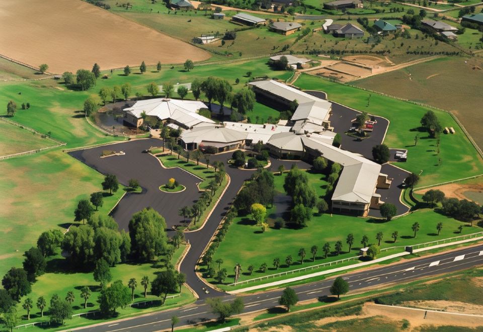 aerial view of a large building surrounded by green grass and trees , with a road leading to it at Parklands Resort Mudgee