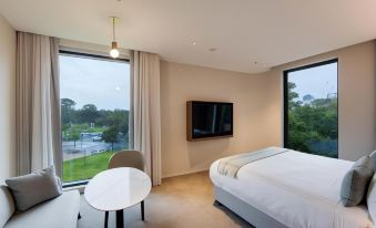 a modern bedroom with a large window , white bed , and a flat - screen tv on the wall at Oval Hotel at Adelaide Oval, an EVT hotel