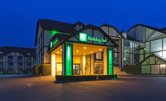 a large green and white holiday inn hotel at night , with the building lit up against a dark blue sky at Holiday Inn Selma-Swancourt