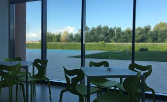 a dining room with green chairs and tables , situated next to a large window that overlooks a golf course at Inn Naples Airport