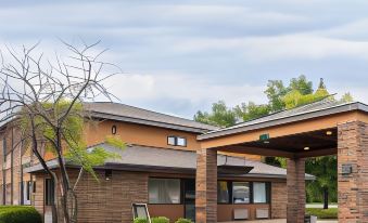 a brick building with a covered walkway and trees in front of it , under a cloudy sky at Days Inn by Wyndham Stoughton WI.