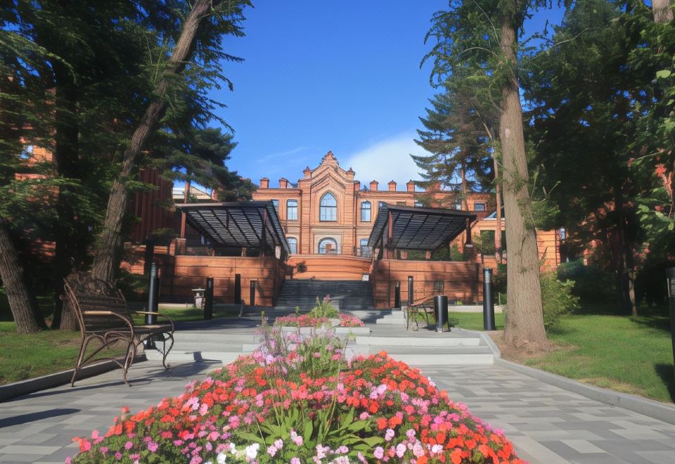 a red brick building surrounded by trees and flowers , with a paved walkway leading up to it at Hotel Parus