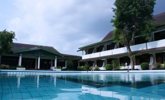 a large swimming pool is surrounded by a modern building with multiple balconies and trees at Kusuma Sahid Prince Hotel Solo