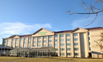 a large hotel building with multiple stories and windows , surrounded by a grassy field under a clear blue sky at Wyndham Garden Manassas