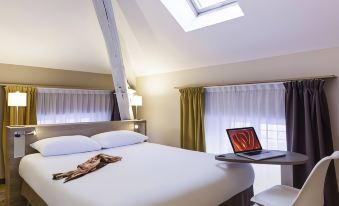 a hotel room with a white bed , a laptop on a desk , and a window with curtains at Ibis Styles Chaumont Centre Gare