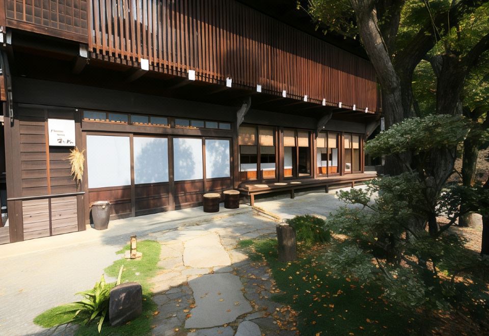 a wooden building with large windows and a stone walkway leading to it , surrounded by trees at Fuefukigawa Onsen Zabou