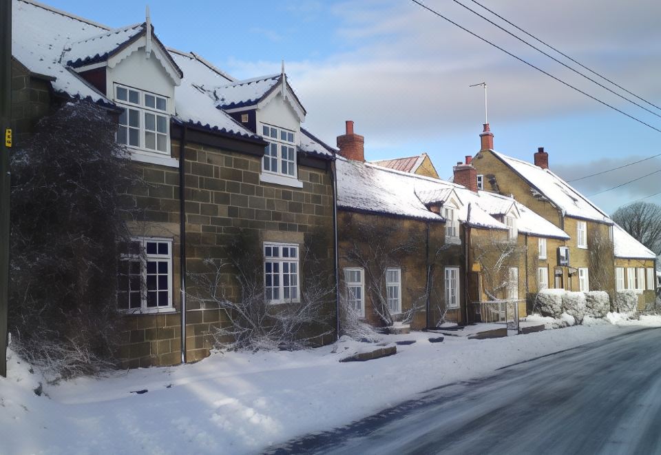 a snow - covered street with several houses , including one with white windows and a brick facade at Ellerby Country Inn