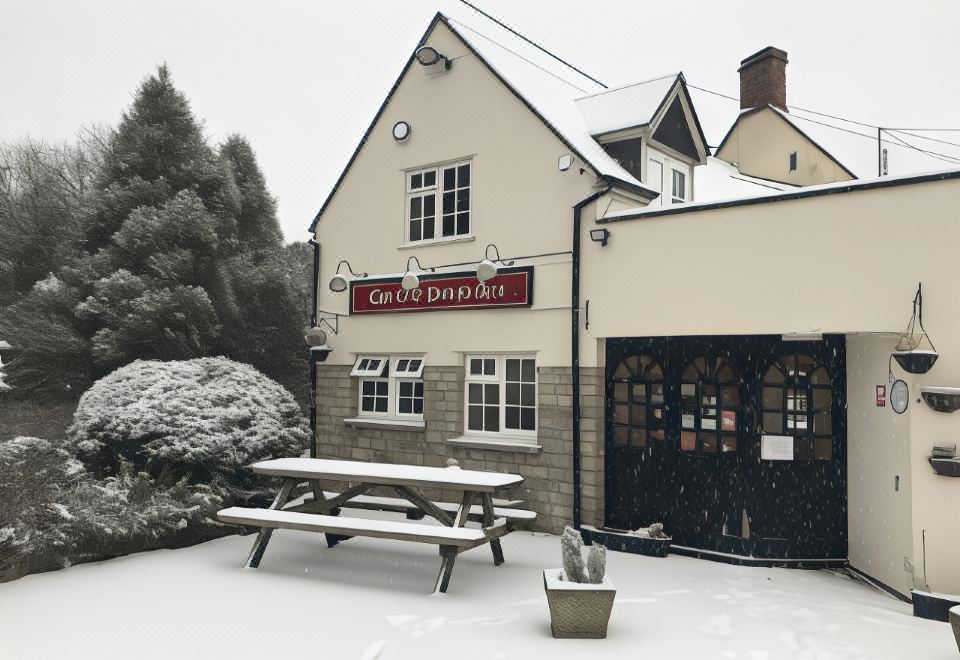 a snow - covered courtyard with a building and a bench in front of it , surrounded by trees at The Old Pound Inn