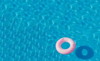 a pink inner tube floating in a blue swimming pool , with the water 's surface shiny and bright at Citihub Hotel @Kediri